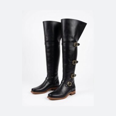 Black leather cavalier thigh-high boots with fold-over bucket cuff and brass buckle straps — three-quarter view